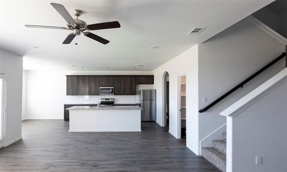 Kitchen featuring dark brown cabinetry, ceiling fan, stainless steel appliances, dark hardwood / wood-style flooring, and a center island with sink