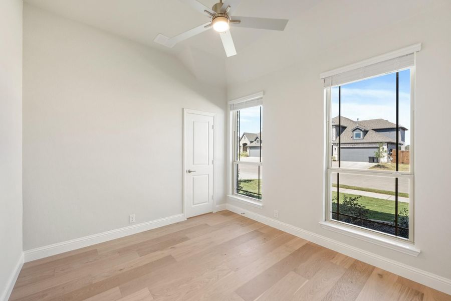 Empty bedroom with vaulted ceiling, ceiling fan, hardwood floors, and two windows overlooking neighborhood homes. Empty bedroom with vaulted ceiling, ceiling fan, hardwood floors, and two windows overlooking neighborhood homes.