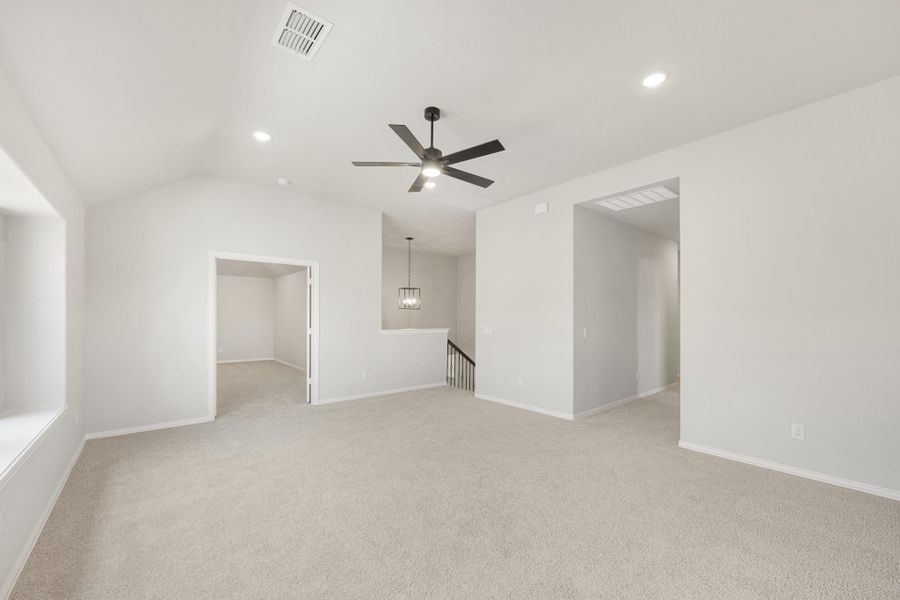 Open upstairs living area with vaulted ceiling, ceiling fan, carpet, and staircase landing nearby.