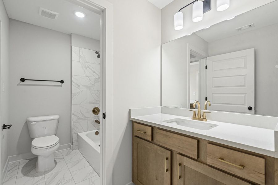 Full bathroom featuring a white vanity with a light-toned countertop, a gold-toned faucet, and a large mirror Full bathroom featuring a white vanity with a light-toned countertop, a gold-toned faucet, and a large mirror