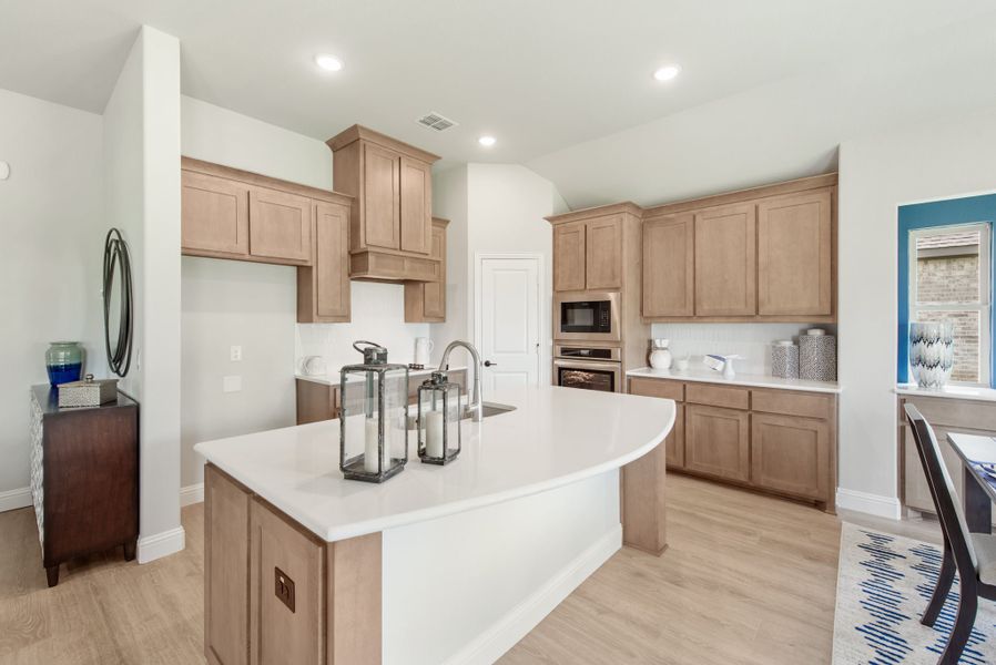 Kitchen with light wood cabinets, white countertop island, stainless steel appliances, and light hardwood floors