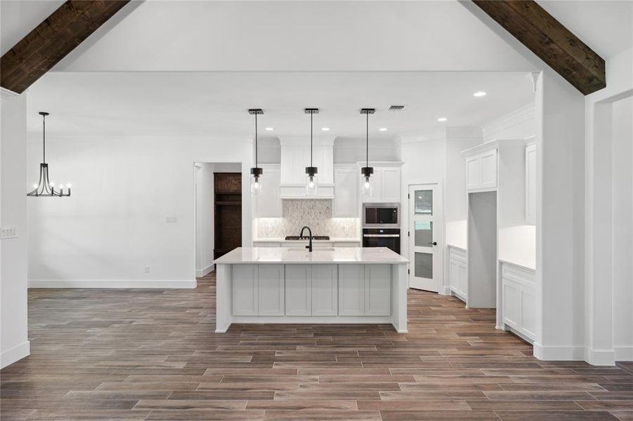 Kitchen featuring a kitchen island with sink, pendant lighting, backsplash, and stainless steel appliances