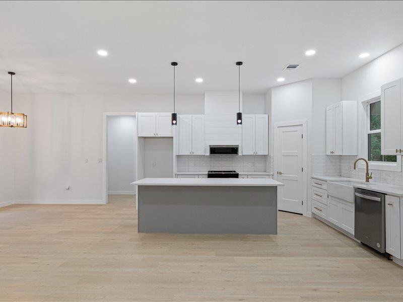 Spacious kitchen featuring an island with a light-colored countertop, white cabinetry, stainless steel appliances, and light-colored flooring throughout