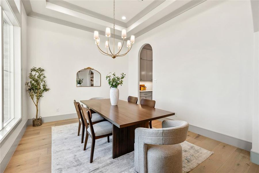 Dining space featuring a raised ceiling, arched walkways, light wood-style flooring, and hanging lights Dining space featuring a raised ceiling, arched walkways, light wood-style flooring, and hanging lights