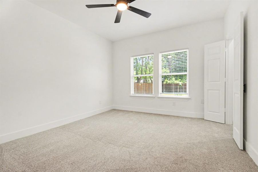 Spacious room featuring light-colored carpeting, white walls, and a ceiling fan