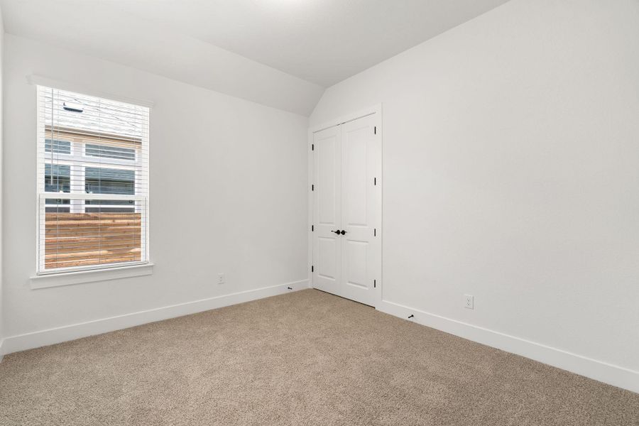 A well-lit bedroom features carpeting and a large window.