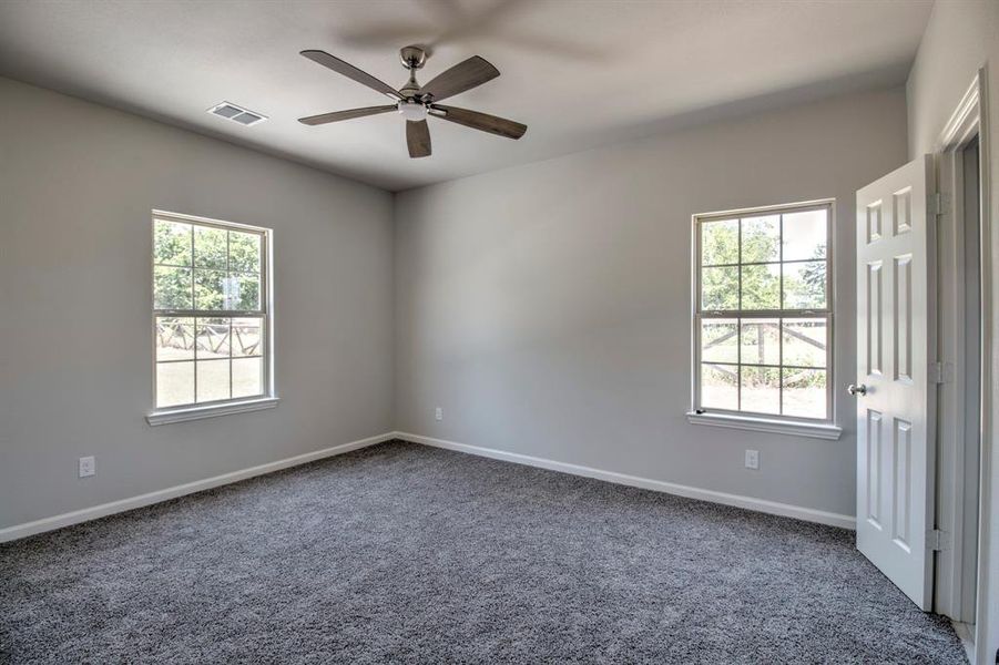 Empty room with carpet flooring, ceiling fan, and a healthy amount of sunlight