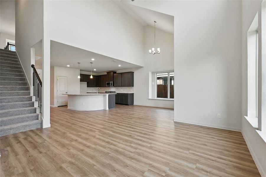 Unfurnished living room featuring stairway, a towering ceiling, light wood finished floors, and a chandelier