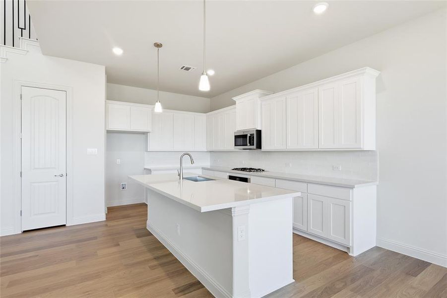 Kitchen with white cabinetry, a center island with sink, light wood-type flooring, stainless steel microwave, and decorative light fixtures
