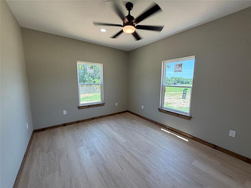 Neutral-toned bedroom featuring two windows, wood-finish flooring, and a ceiling fan with integrated lighting
