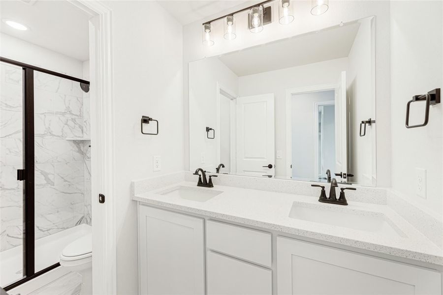 Bathroom with double vanity, white quartz countertop, black fixtures, and marble tile walk-in shower with glass door