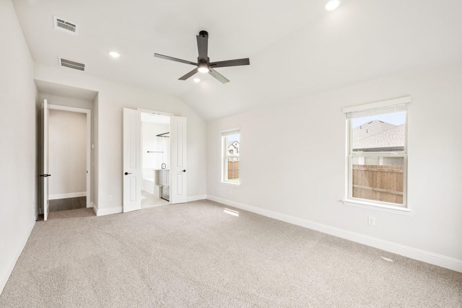 Empty bedroom with vaulted ceiling, ceiling fan, carpet flooring, and doors leading to closet and ensuite bathroom Empty bedroom with vaulted ceiling, ceiling fan, carpet flooring, and doors leading to closet and ensuite bathroom