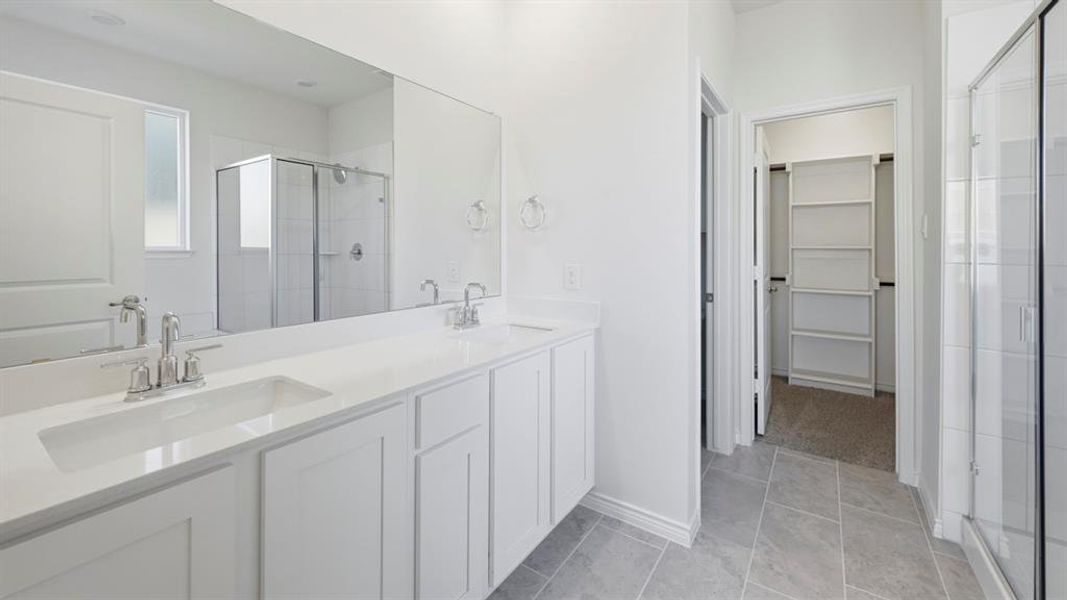 Full bathroom featuring a walk in closet, a shower stall, double vanity, and light tile patterned floors