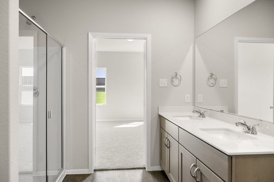 Image of home primary bathroom with vanity with white countertop and light brown cabinets and mirror, and doorway to bedroom with walk-in shower