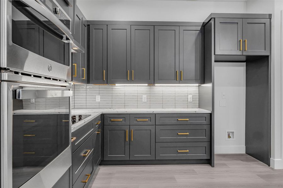 Stylish kitchen featuring a stainless steel double oven, decorative backsplash, light wood-style flooring, baseboards, and sleek gray cabinets. Stylish kitchen featuring a stainless steel double oven, decorative backsplash, light wood-style flooring, baseboards, and sleek gray cabinets.