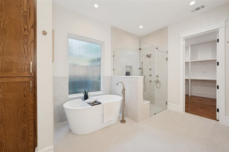 Freestanding soaking tub with floor-mounted faucet, oversized glass-enclosed shower with multiple sprayers, wood-paneled built-in storage cabinetry, and recessed lighting