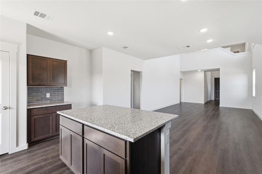 Kitchen with dark brown cabinetry, tasteful backsplash, light stone countertops, a kitchen island, and dark wood-style flooring Kitchen with dark brown cabinetry, tasteful backsplash, light stone countertops, a kitchen island, and dark wood-style flooring