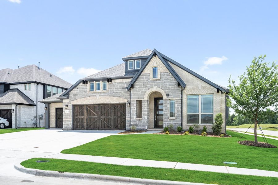 Stone and brick home with two-car garage, arched entry, and manicured front lawn