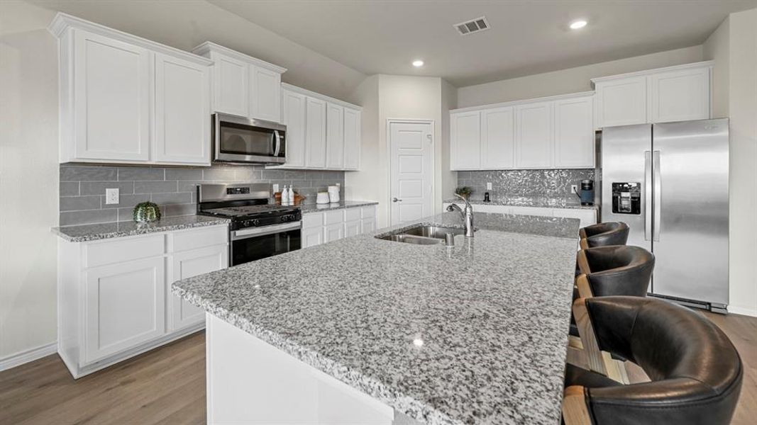 Kitchen featuring appliances with stainless steel finishes, decorative backsplash, light stone countertops, white cabinets, and recessed lighting