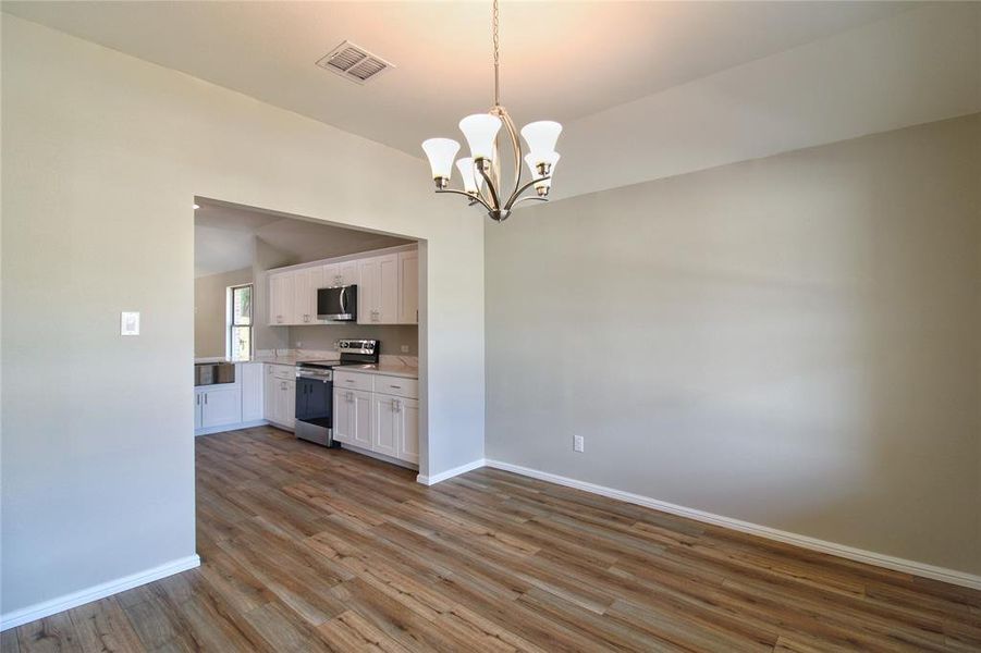 Kitchen with dark wood-style flooring, appliances with stainless steel finishes, white cabinetry, a chandelier, and hanging light fixtures
