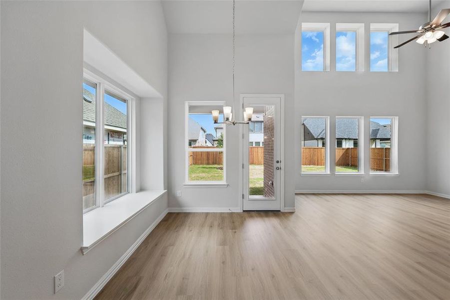 Unfurnished dining area with light wood-type flooring, plenty of natural light, ceiling fan, suspended lighting, and a high ceiling