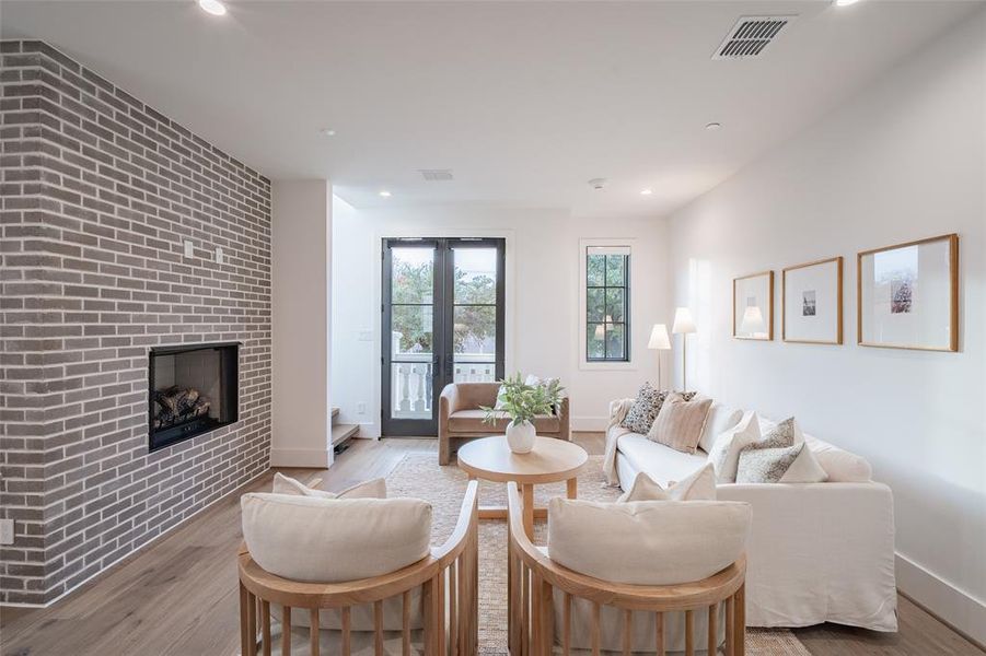 Living room with brick wall, a fireplace, and light wood-type flooring