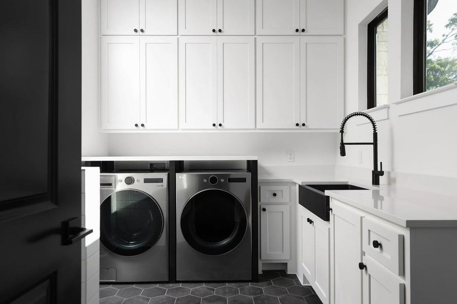 Laundry room featuring white shaker cabinetry with black hardware, hexagon tile flooring, a black farmhouse-style sink with a matte black pull-down faucet, and light-toned countertops
