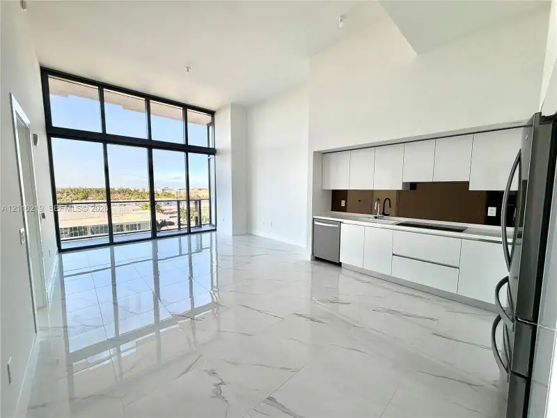 Open-concept floor plan featuring floor-to-ceiling windows, polished tile flooring, white slab-front cabinetry, and a dark reflective backsplash