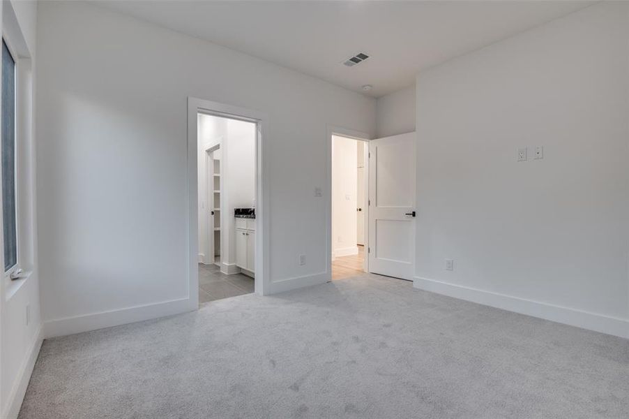 Unfurnished bedroom featuring light carpet and ensuite bath Unfurnished bedroom featuring light carpet and ensuite bath