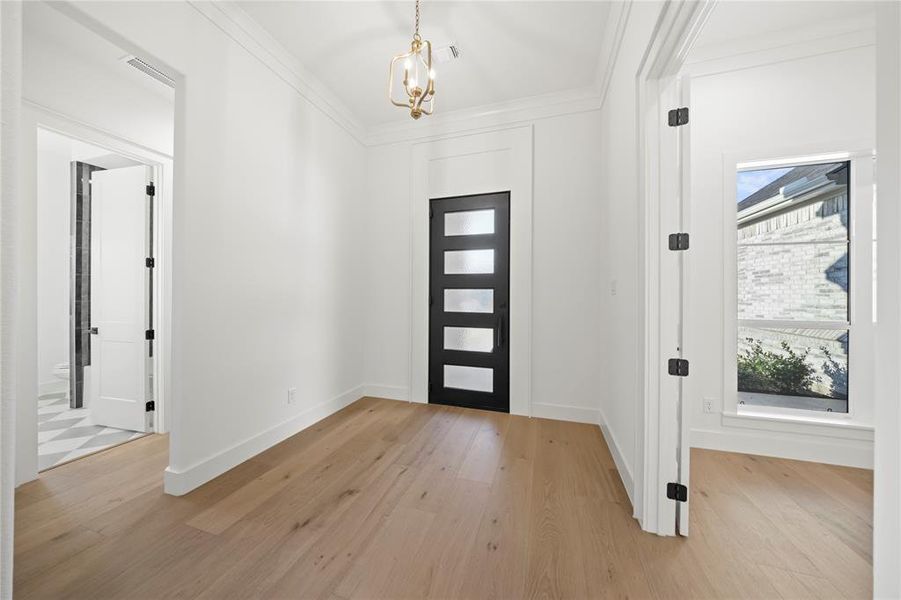 Bright hallway featuring light wood-finish flooring, a modern five-panel door with frosted glass inserts, and a decorative brass chandelier