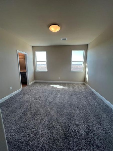 Unfurnished bedroom with dark colored carpet, multiple windows, visible vents, and baseboards