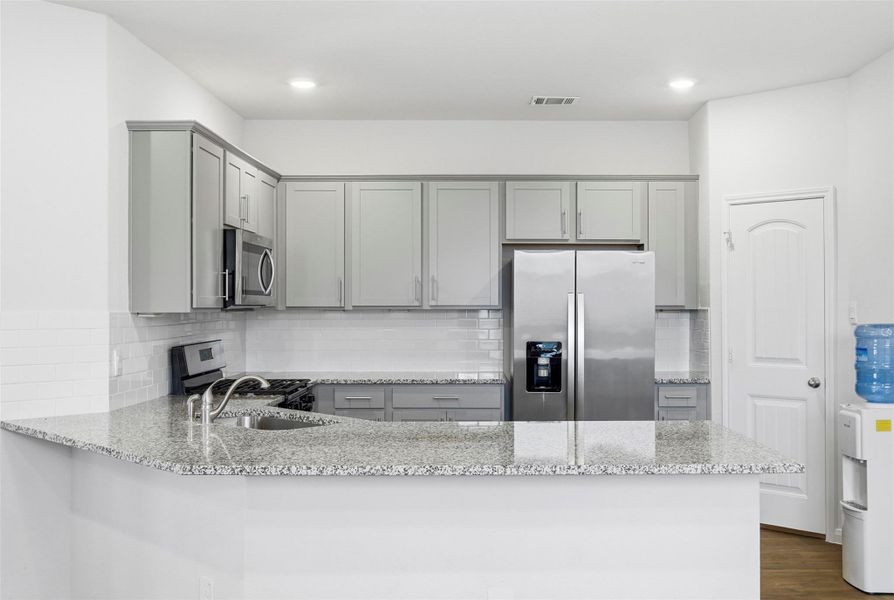Kitchen with gray cabinets, light stone counters, appliances with stainless steel finishes, and recessed lighting Kitchen with gray cabinets, light stone counters, appliances with stainless steel finishes, and recessed lighting