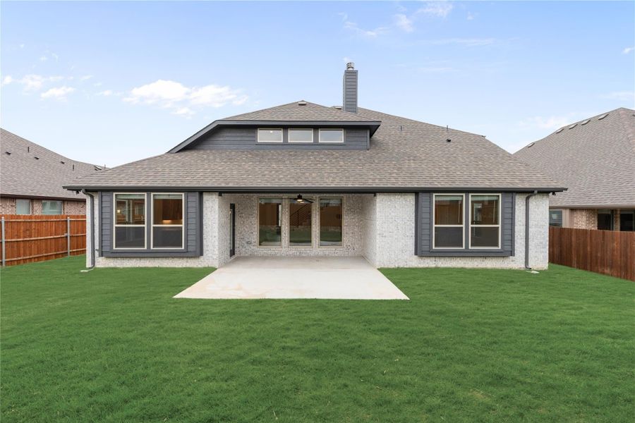 Rear exterior of single-story brick home with covered patio, large windows, and fenced backyard with green lawn