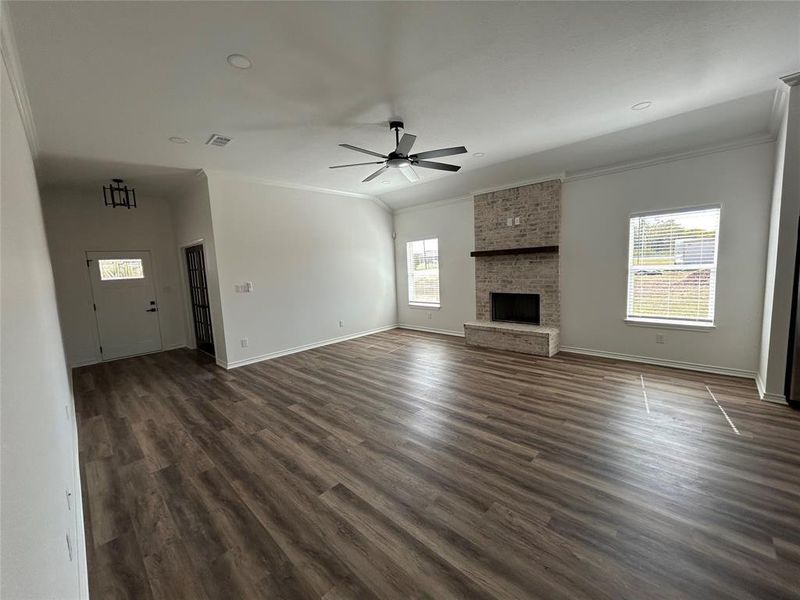 Unfurnished living room with crown molding, dark wood-style floors, ceiling fan, and a fireplace