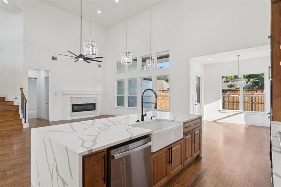 Kitchen featuring stained brown cabinets, dark real-wood floors, stainless steel dishwasher, a kitchen island with sink, and recessed lighting