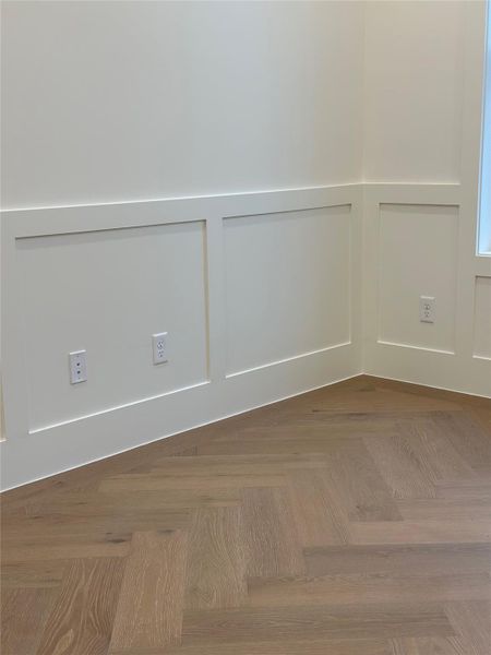 A dedicated home office featuring detailed wainscoting and herringbone wood flooring, softened by natural light that fills the room throughout the day.