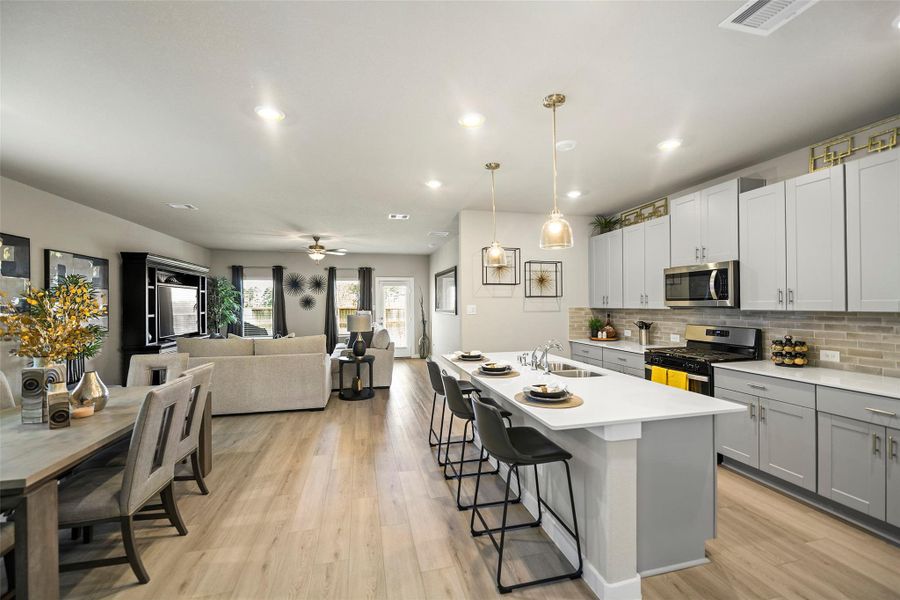 Bright and open-concept living space features a modern kitchen with sleek gray cabinetry and a large island, seamlessly flowing into a cozy living area perfect for entertaining.