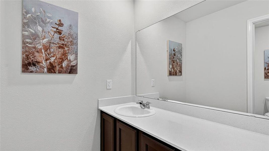 Bathroom vanity featuring a built-in sink with a chrome faucet, solid surface countertop, dark wood-finish cabinetry, and a full-width mirror Bathroom vanity featuring a built-in sink with a chrome faucet, solid surface countertop, dark wood-finish cabinetry, and a full-width mirror