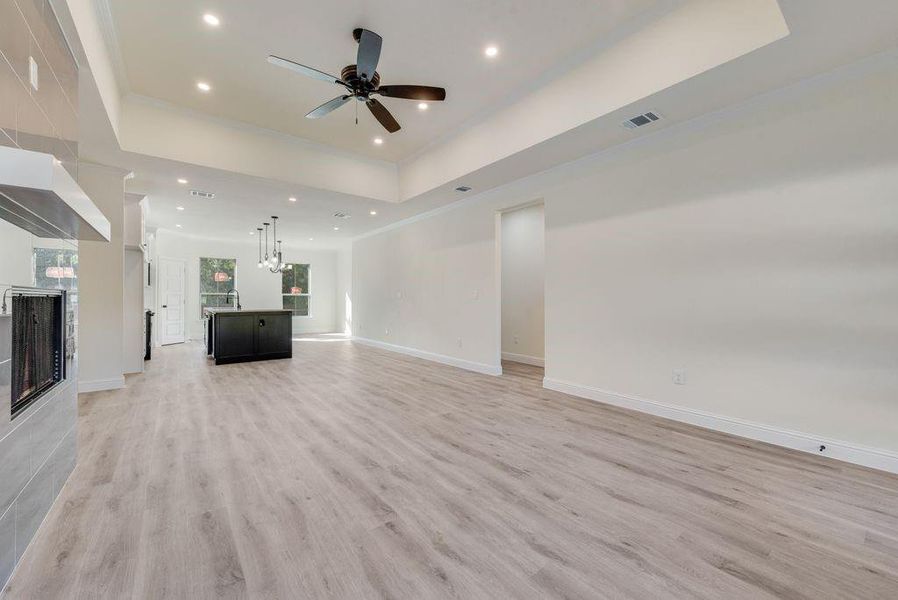 Unfurnished living room with ceiling fan with notable chandelier, a tray ceiling, and light wood-type flooring