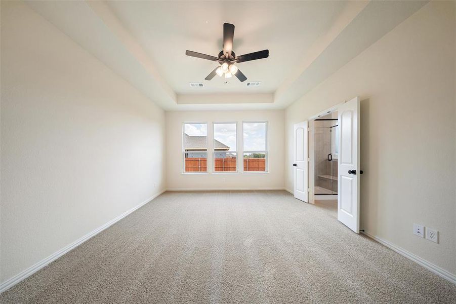 Unfurnished bedroom with light colored carpet, a tray ceiling, and ceiling fan