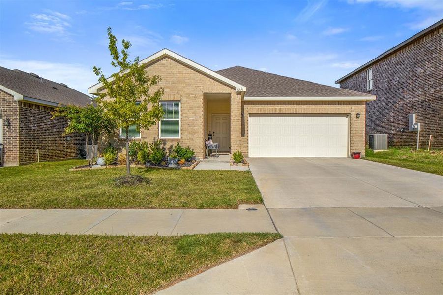 Single story home with brick siding, an attached garage, concrete driveway, a front yard, and roof with shingles