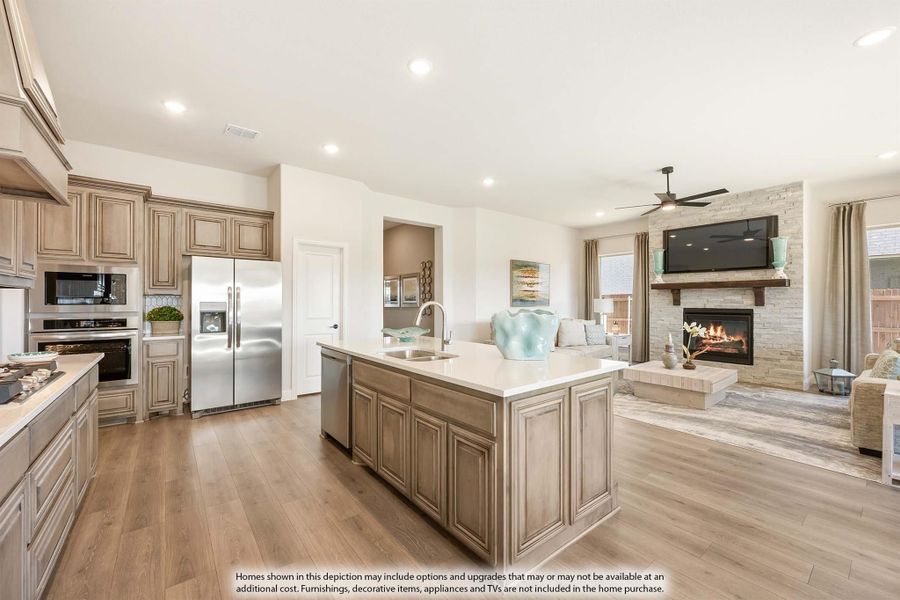 Open kitchen with large center island, stainless appliances, and wood floors flowing into living room with stone fireplace Open kitchen with large center island, stainless appliances, and wood floors flowing into living room with stone fireplace