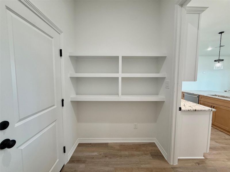 Built-in shelving unit with five white shelves, contrasting against a white painted wall and wood-finish flooring