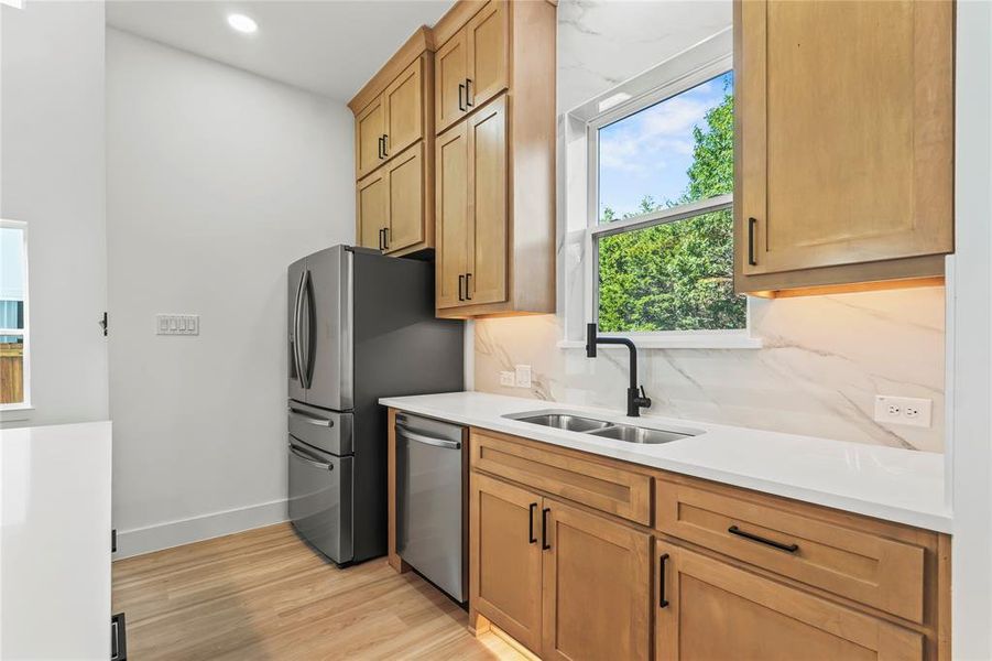 Kitchen featuring light wood-style flooring, stainless steel dishwasher, and light stone counters