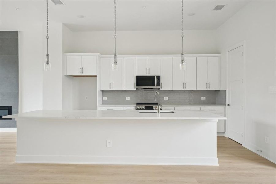 Kitchen featuring stainless steel microwave, a kitchen island with sink, white cabinetry, and backsplash