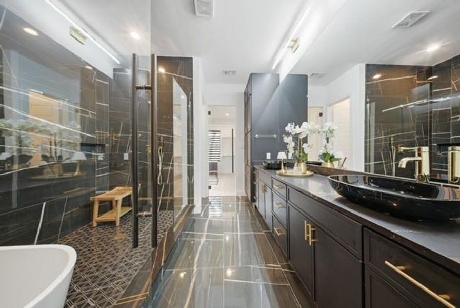 Spacious Primary bathroom featuring dark marble-effect wall and floor tiling, a dual vanity with a dark countertop and vessel sinks, gold-tone fixtures, and a glass-enclosed shower
