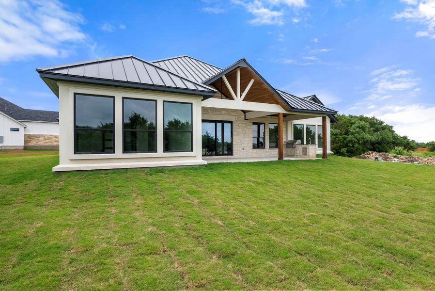 A modern facade with metal roofing and extensive rear-facing windows opens to a sprawling green yard.