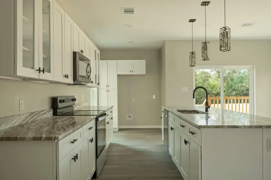 Kitchen featuring stainless steel appliances, light stone countertops, white cabinetry, pendant lighting, and glass insert cabinets