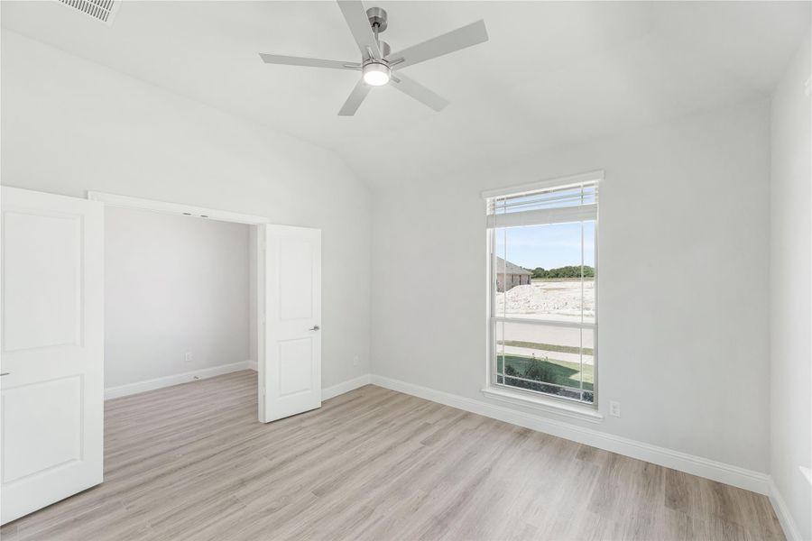 Empty bedroom with vaulted ceiling, ceiling fan, hardwood floors, and large window Empty bedroom with vaulted ceiling, ceiling fan, hardwood floors, and large window