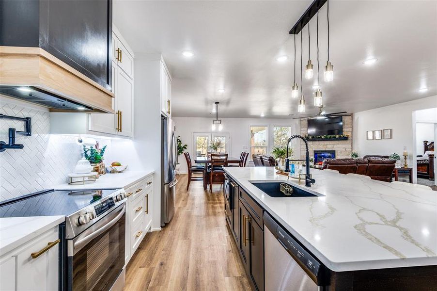 Kitchen featuring white cabinets, appliances with stainless steel finishes, a large island with sink, hanging light fixtures, and recessed lighting
